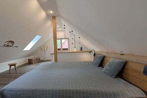 A bedroom with a sloped ceiling, a bed with a grey quilt, a wooden bench, and a skylight. - Country house holiday apartment Lüßvitz (Ummanz)