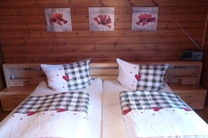 A double bed with a plaid bedspread and heart-patterned pillows, flanked by two bedside tables with lamps. - Holiday home in Seewald with swimming pool (Seewald)