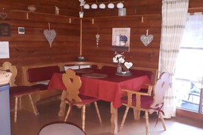 Ein Holzblockhaus-Interieur mit einem Esstisch, der für vier Personen gedeckt ist, umgeben von Holzkästen.