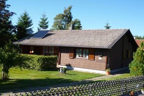 Ein Haus mit geneigtem Dach, Solaranlagen und einem eingezäunten Garten.