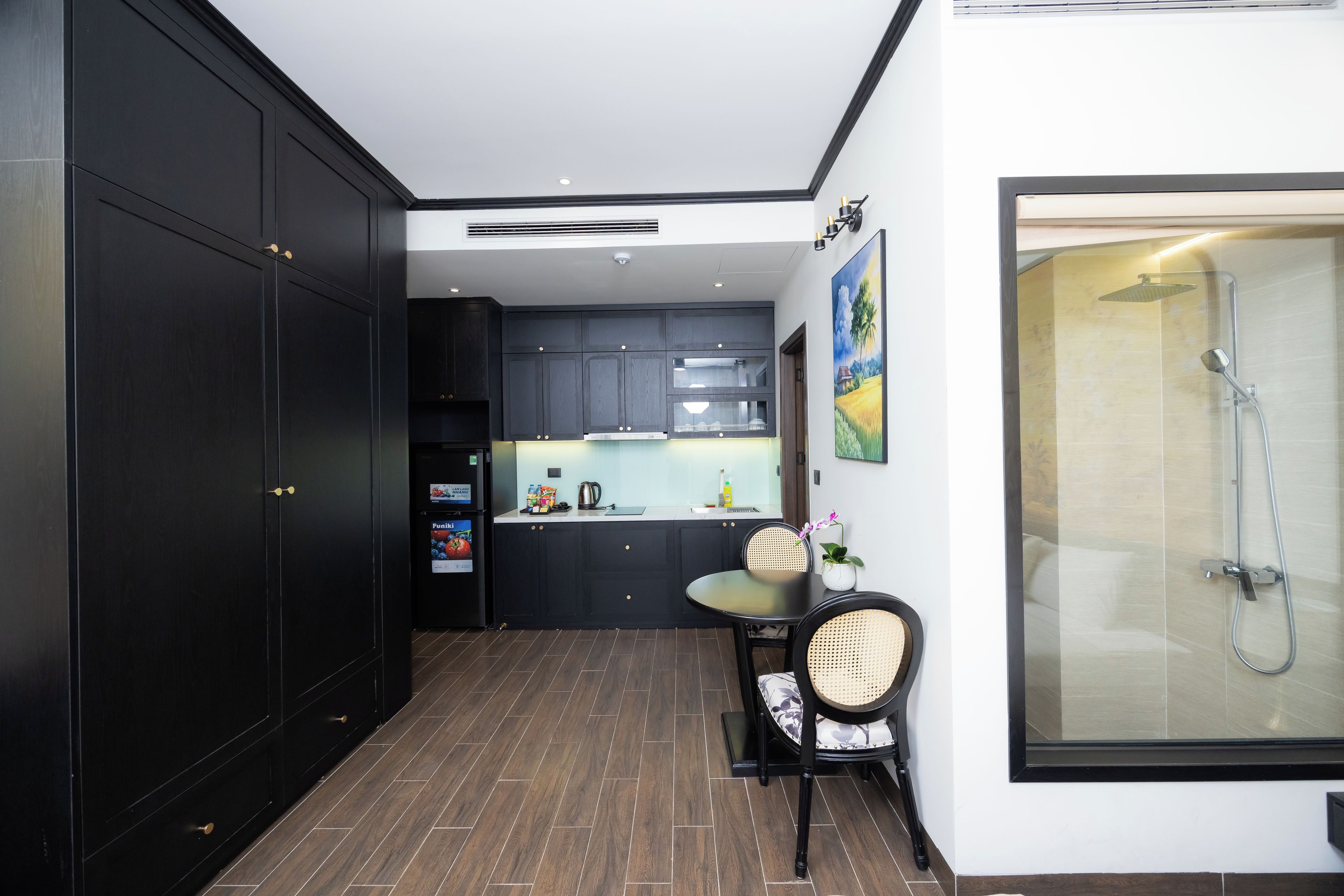 A compact kitchen with dark cabinetry, a dining area with a table and chairs, and a shower area with a glass enclosure.