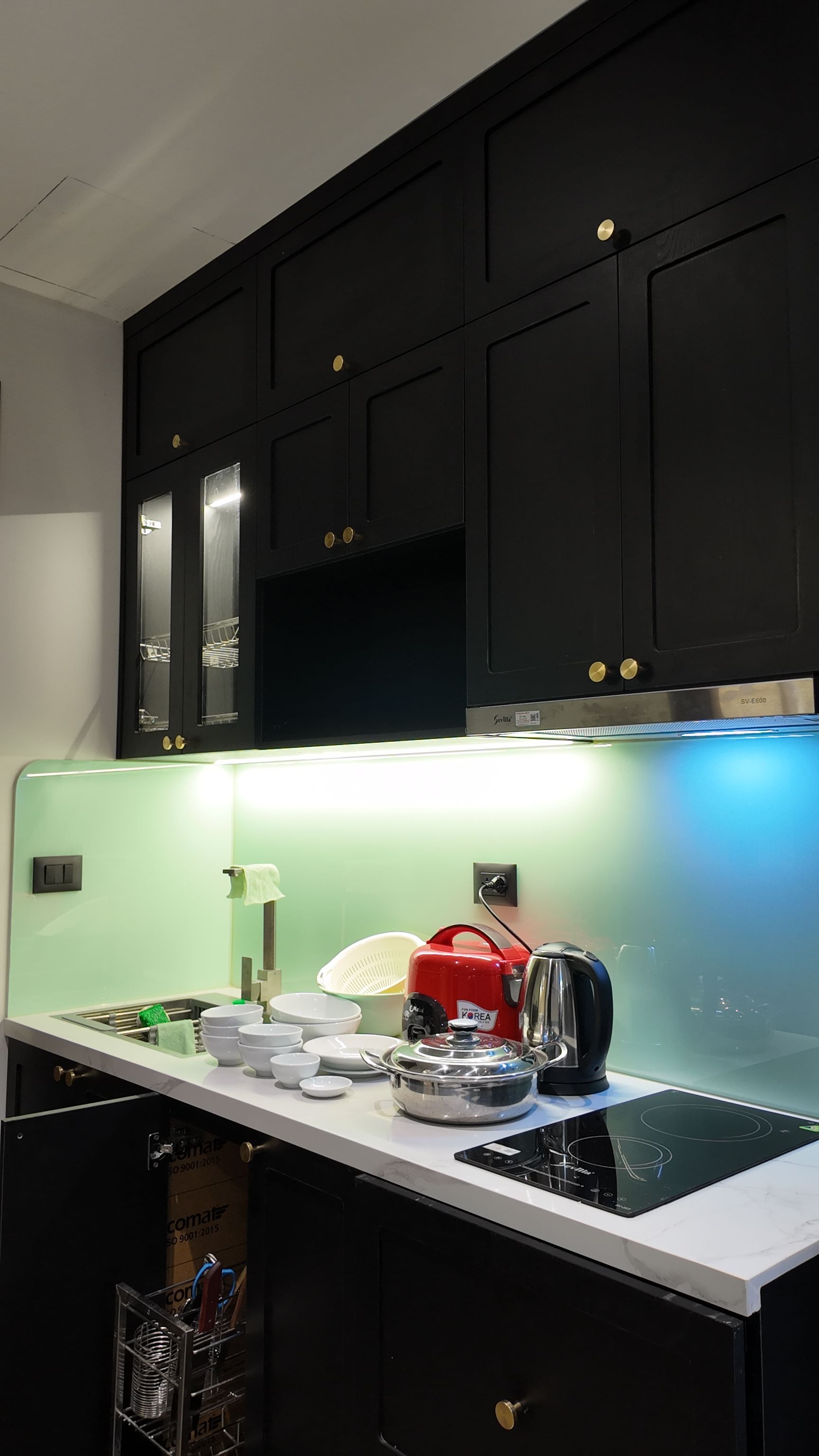 A modern kitchen with black cabinets, a stainless steel range hood, and a white countertop with various kitchen items.
