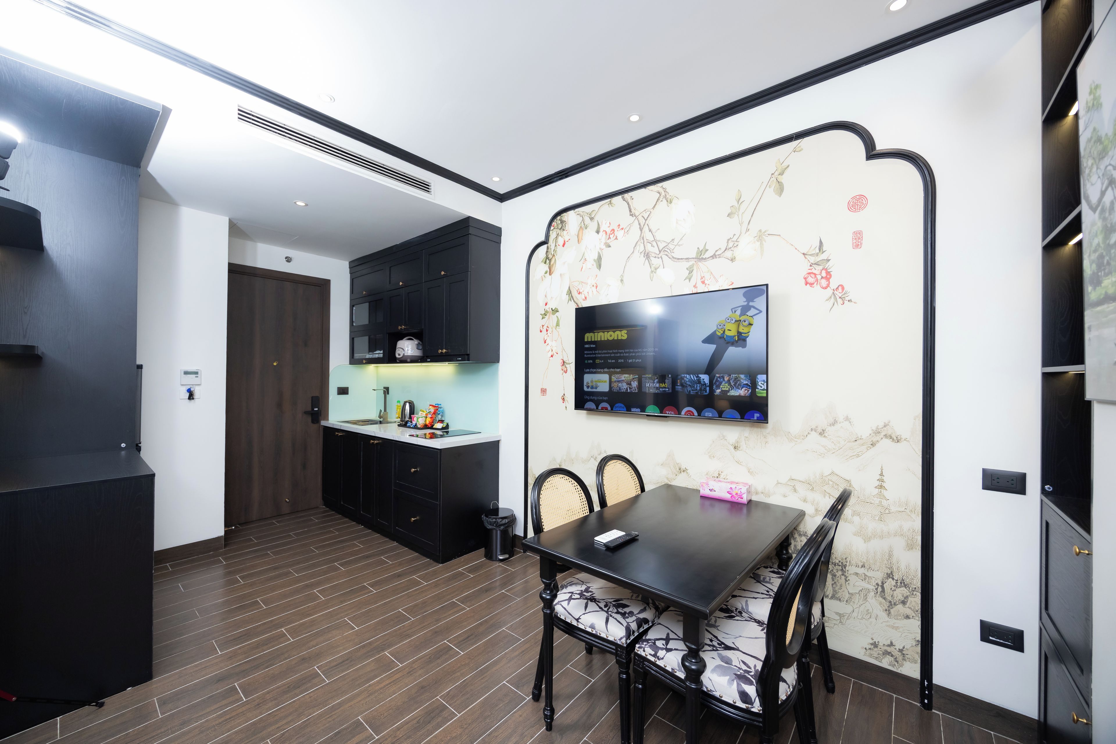 A modern kitchen with a dining area, featuring a large flat-screen TV mounted on the wall.