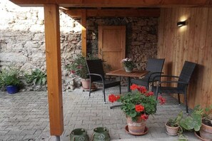 Eine Terrasse im Freien mit einer Steinwand, einer Holz-Pergola und einem Tisch mit Stühlen.