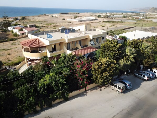 A multi-story building with a rooftop terrace, a parking area with several cars, and a view of the sea in the background.