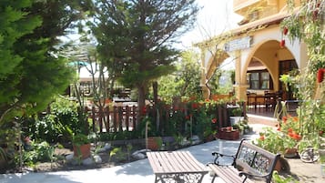 An outdoor seating area with wooden benches and tables, surrounded by greenery and a wooden fence.