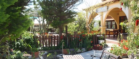 An outdoor seating area with wooden benches and tables, surrounded by greenery and a wooden fence.