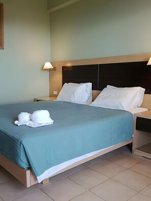 A neatly made bed with a teal bedspread, white pillows, and a white towel on the side.