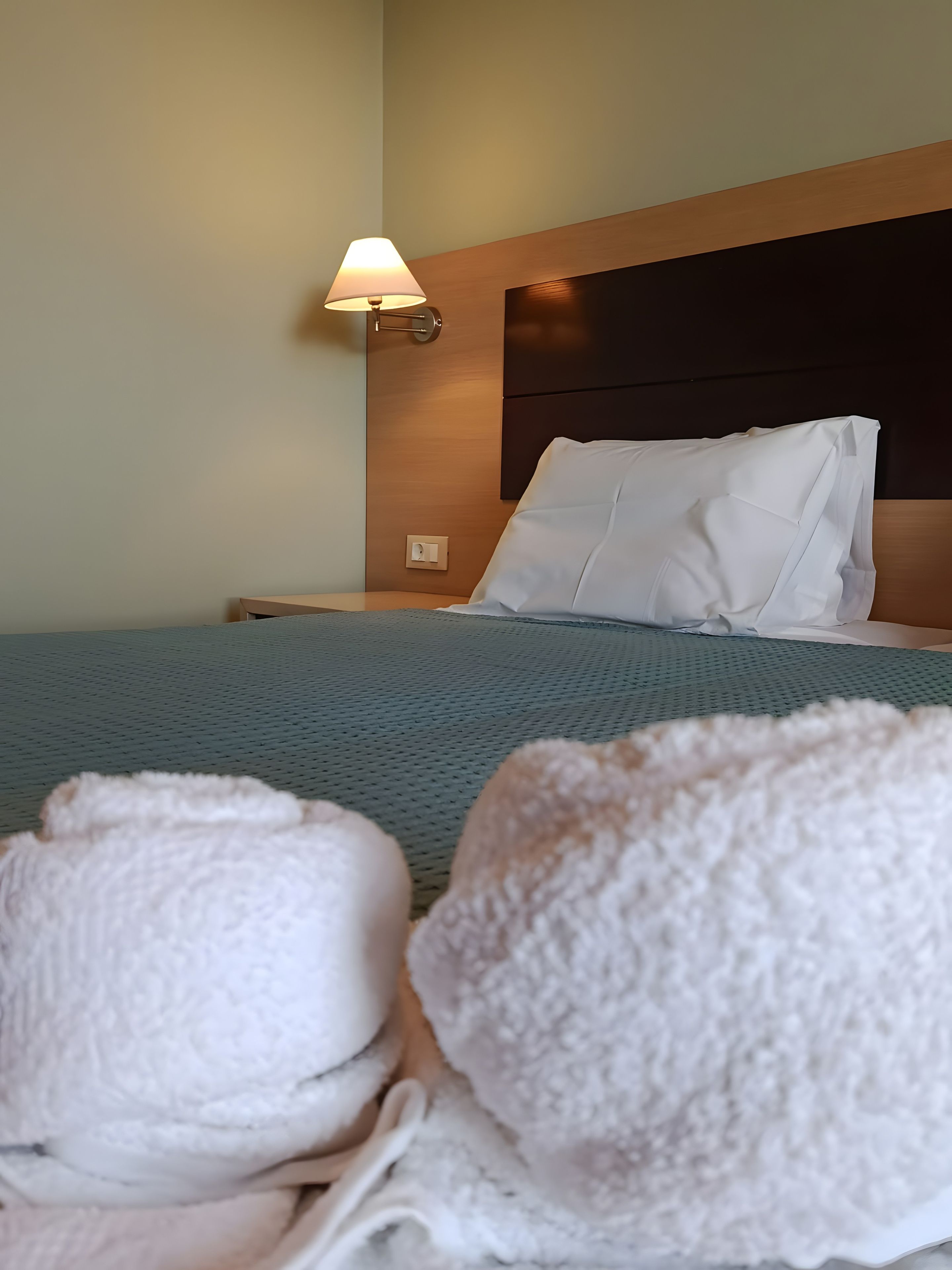 Una habitación de hotel con cama, mesita de noche, lámpara y toallas.