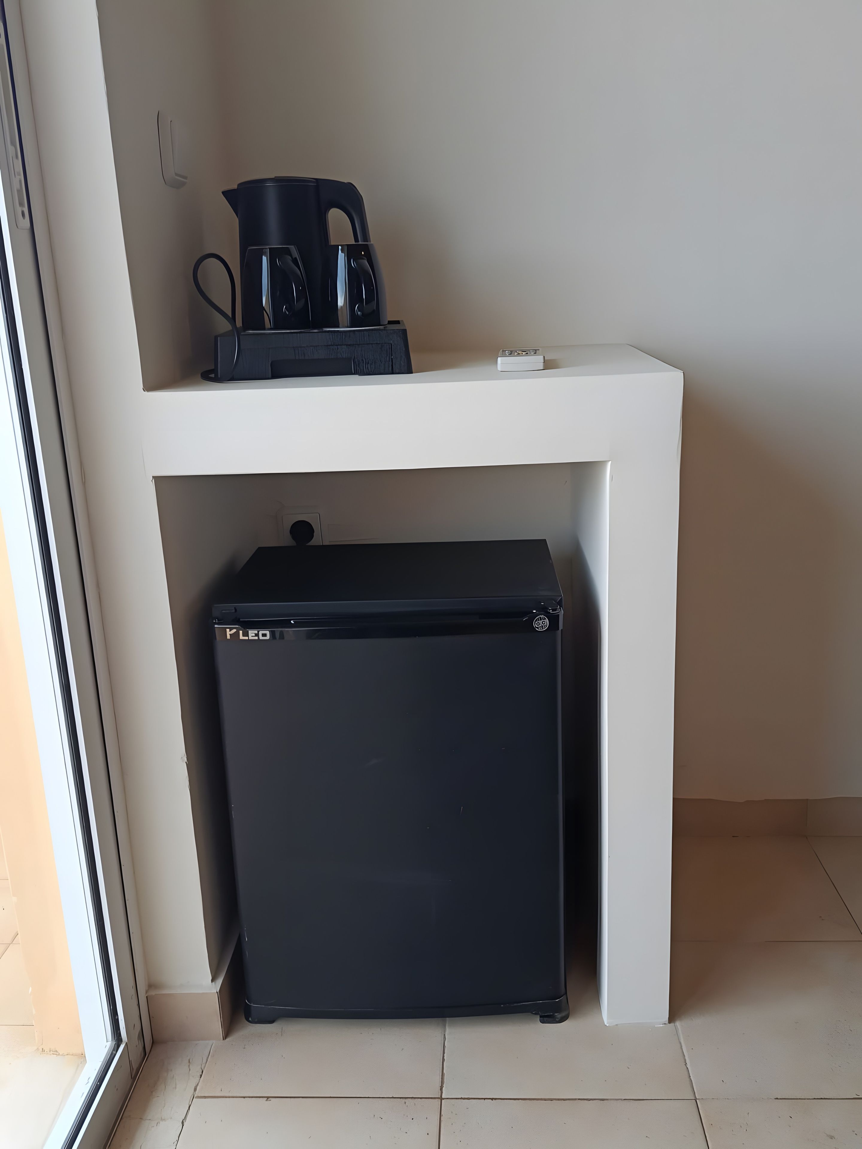 Una kitchenette compacta con un refrigerador negro, una cafetera y una pequeña encimera.