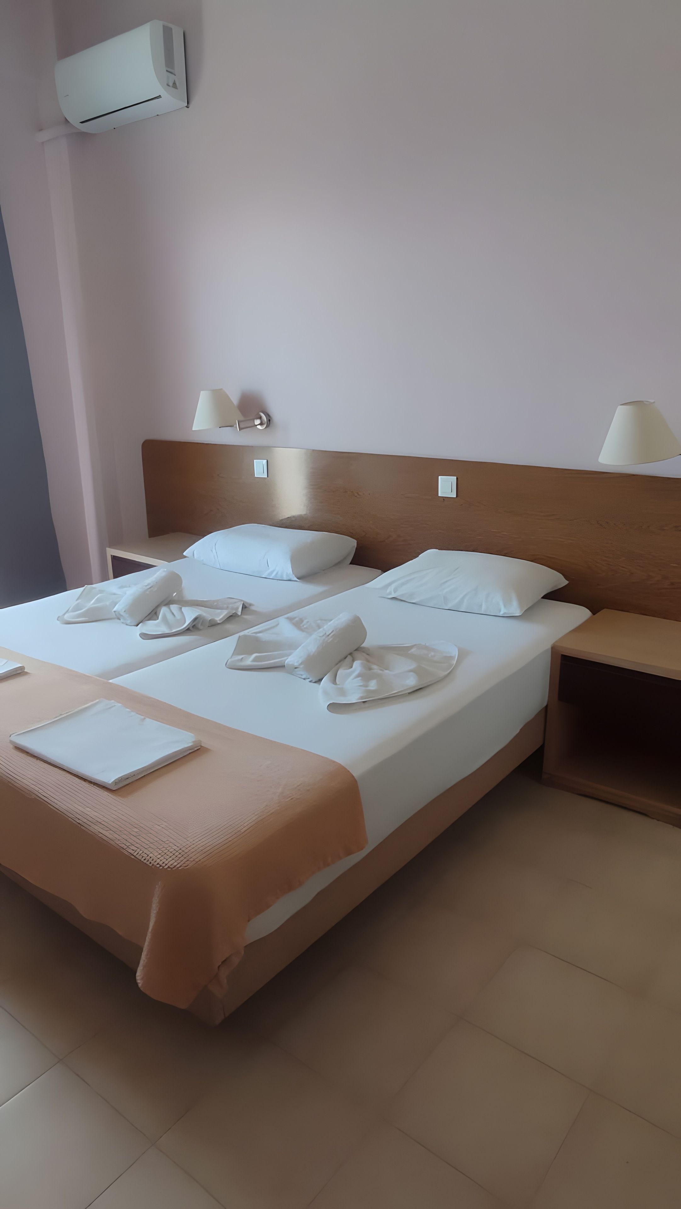 Una habitación de hotel con una cama, dos mesitas de noche, una lámpara y un equipo de aire acondicionado.