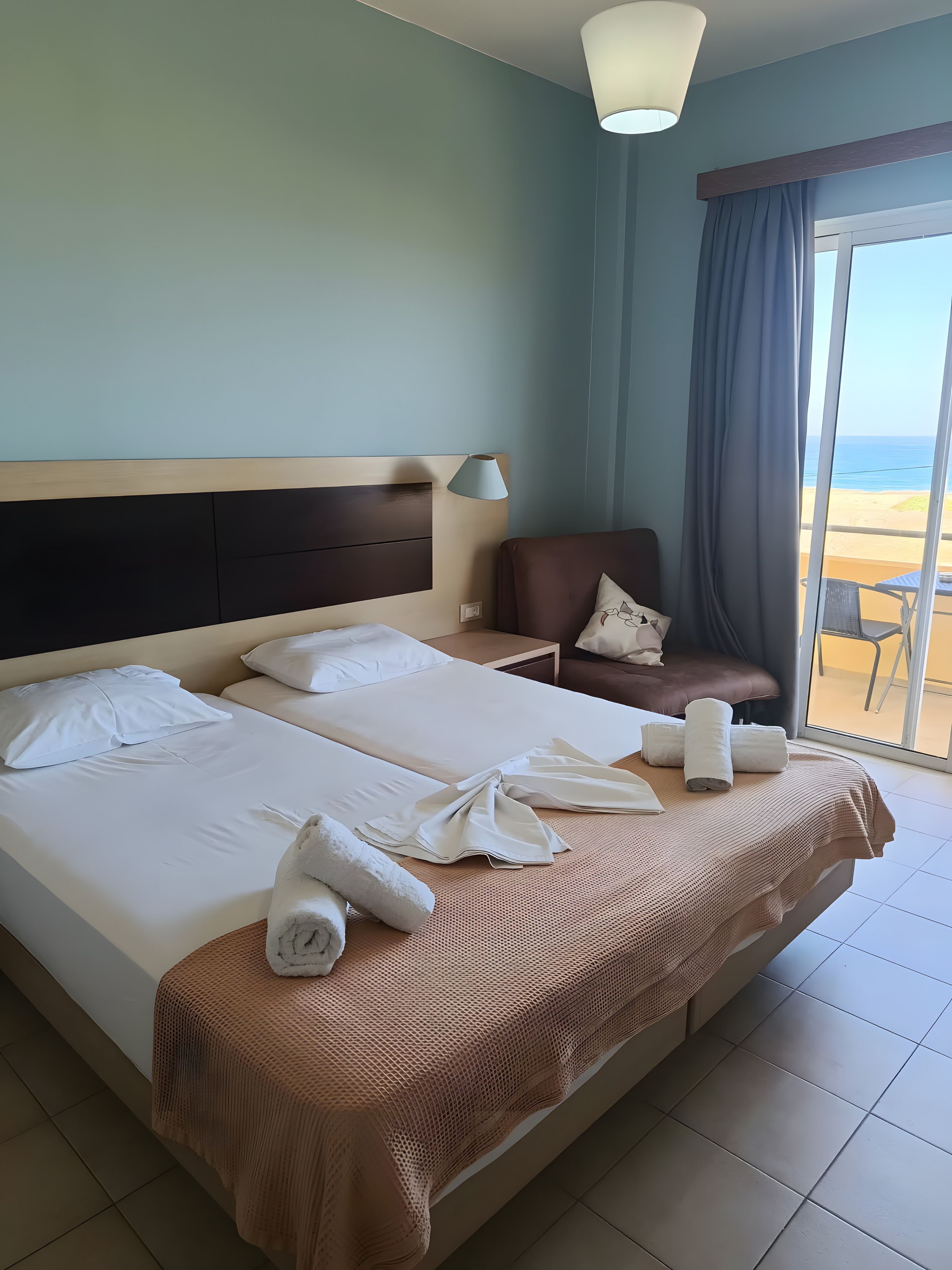 A hotel room with a large bed, a chair, a table, and a view of the beach.