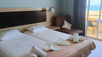 A hotel room with a large bed, a chair, a table, and a view of the beach.