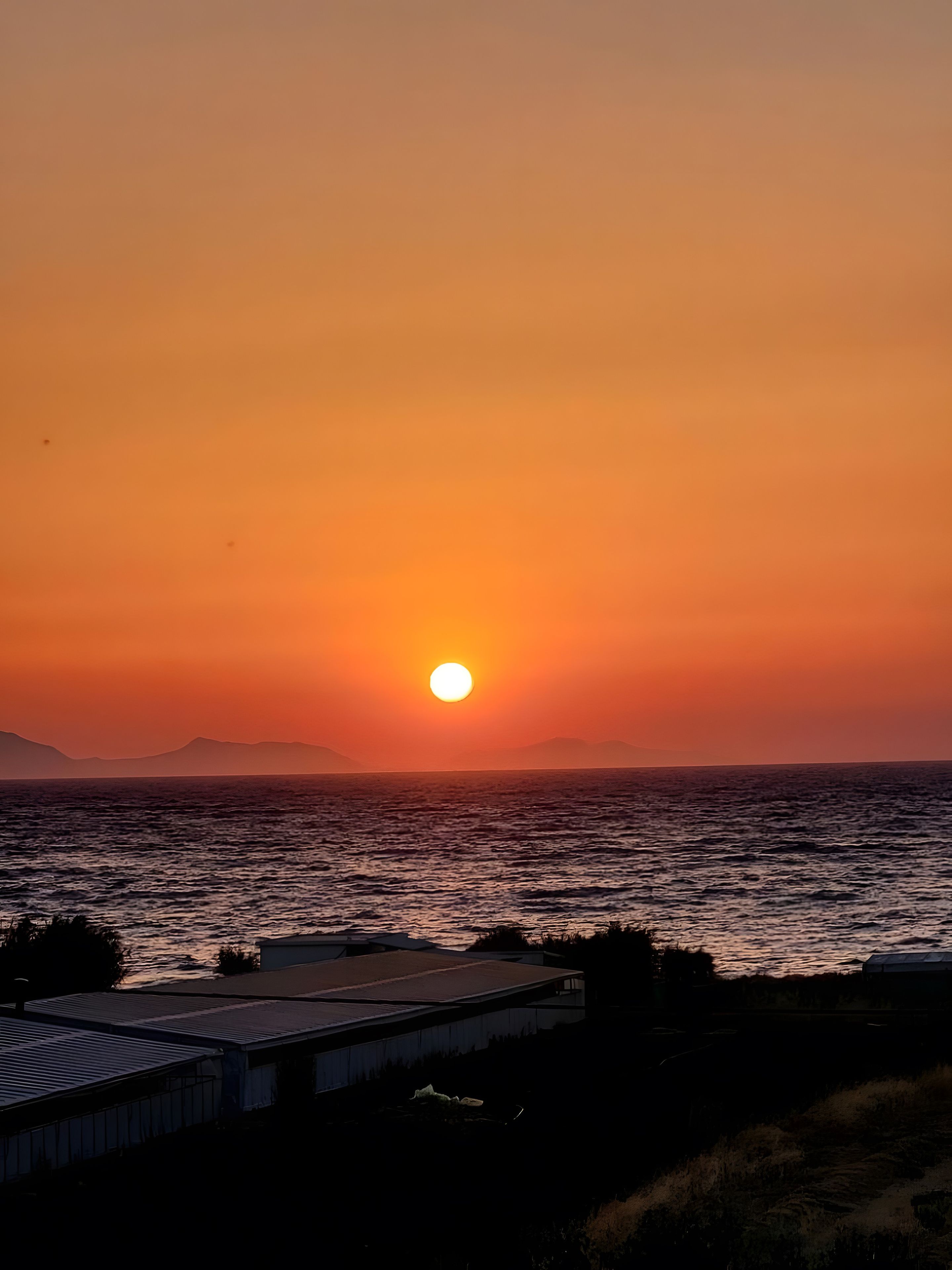A sunset over a body of water with a building in the foreground.