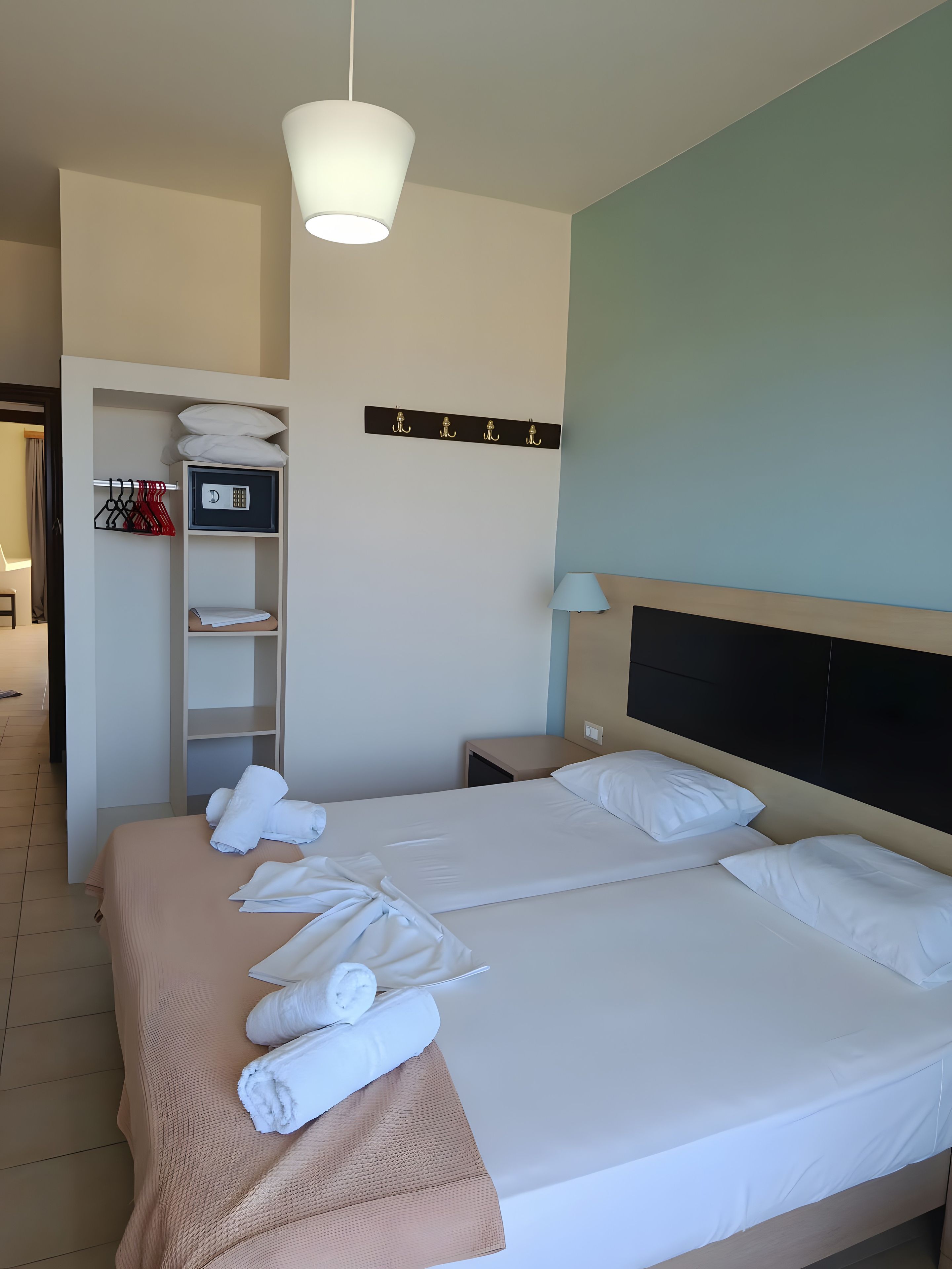 Une chambre d’hôtel comprenant un lit, une table de chevet, une lampe, une armoire et un porte-manteau.