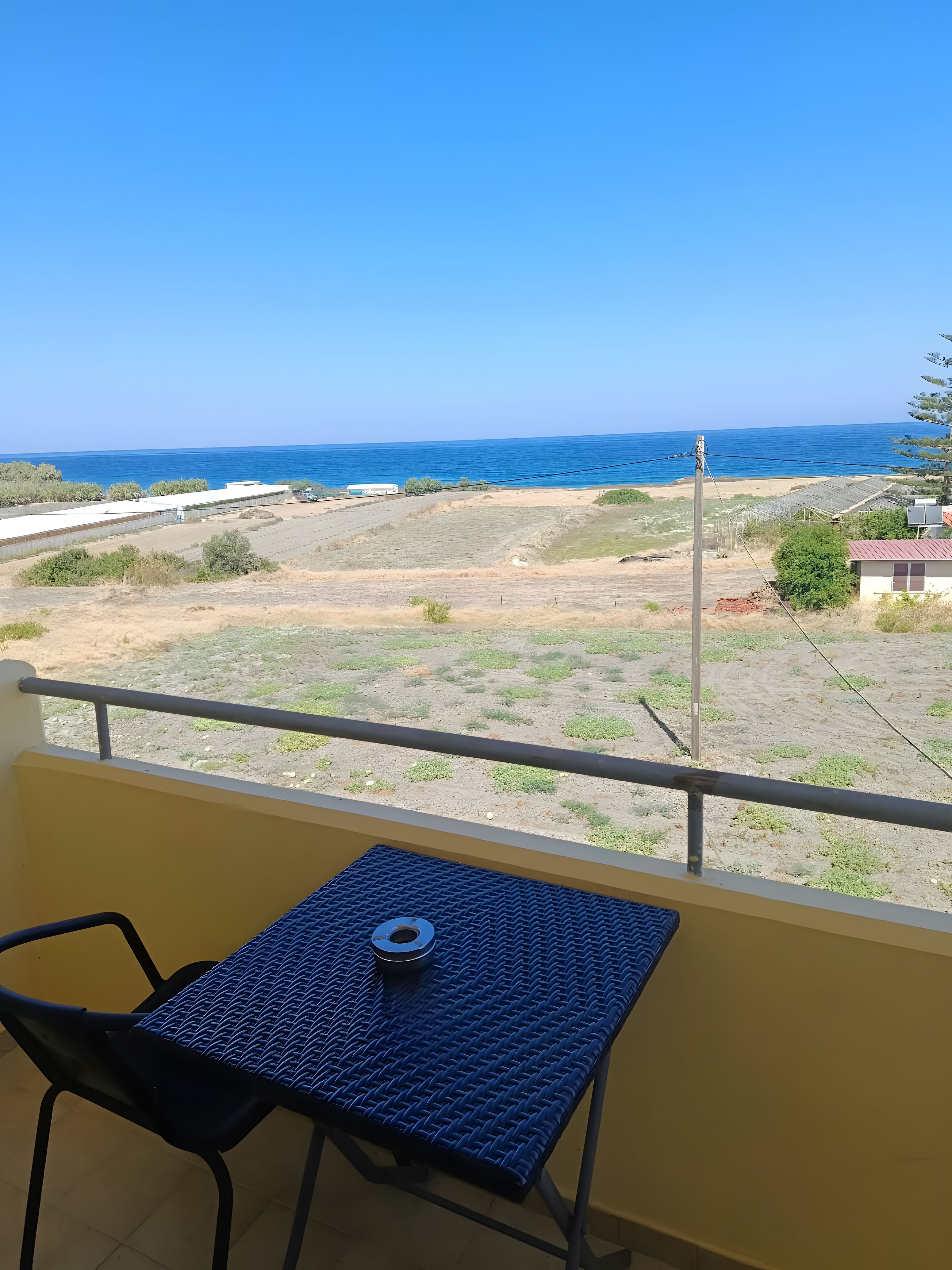 Un balcon avec une table et une chaise, donnant sur une plage et un ciel dégagé.