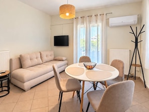 Ein modernes Wohnzimmer mit einer Couch, einem runden Esstisch mit Stühlen, einem Fernseher und einer Klimaanlage.