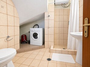 Un baño pequeño con inodoro, lavadora, ducha y lavamanos.