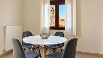 A dining area with a round table and four chairs, a radiator, and a window with curtains.