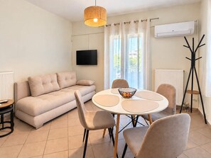 Ein modernes Wohnzimmer mit einer Couch, einem runden Esstisch mit Stühlen, einem Fernseher und einer Klimaanlage.