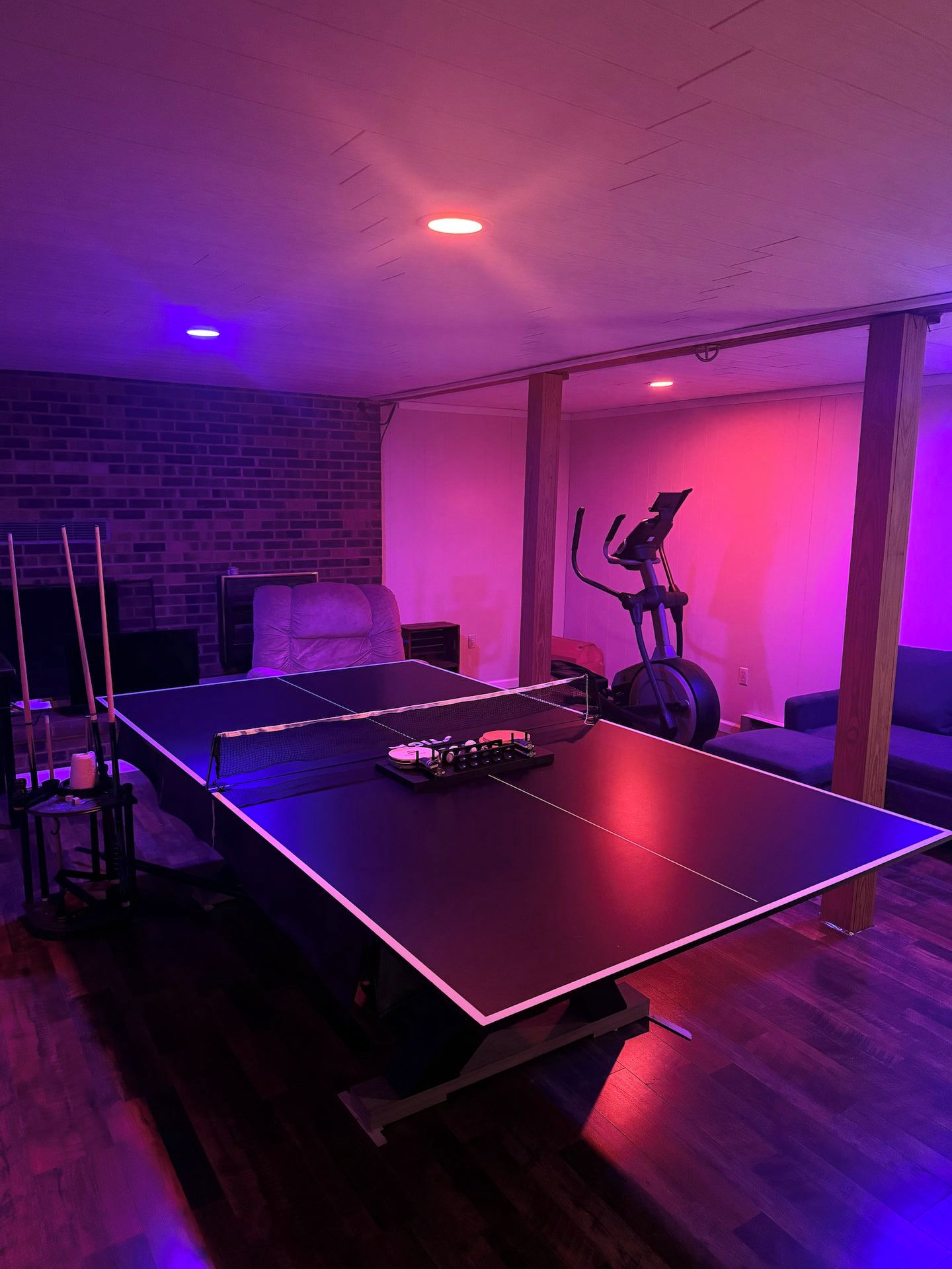 Een kamer met een tafeltennistafel, een hometrainer en een bakstenen muur.