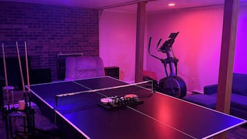 Een kamer met een tafeltennistafel, een hometrainer en een bakstenen muur.