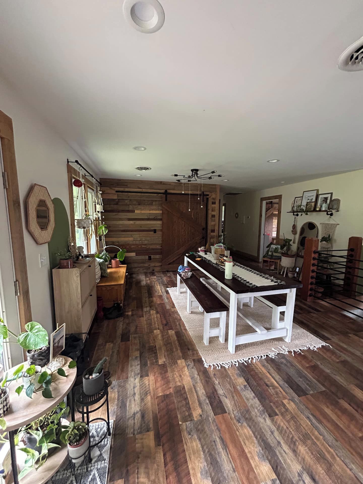 Een ruime kamer met een houten vloer, een eettafel met banken, en een houten wand met een hanglamp.