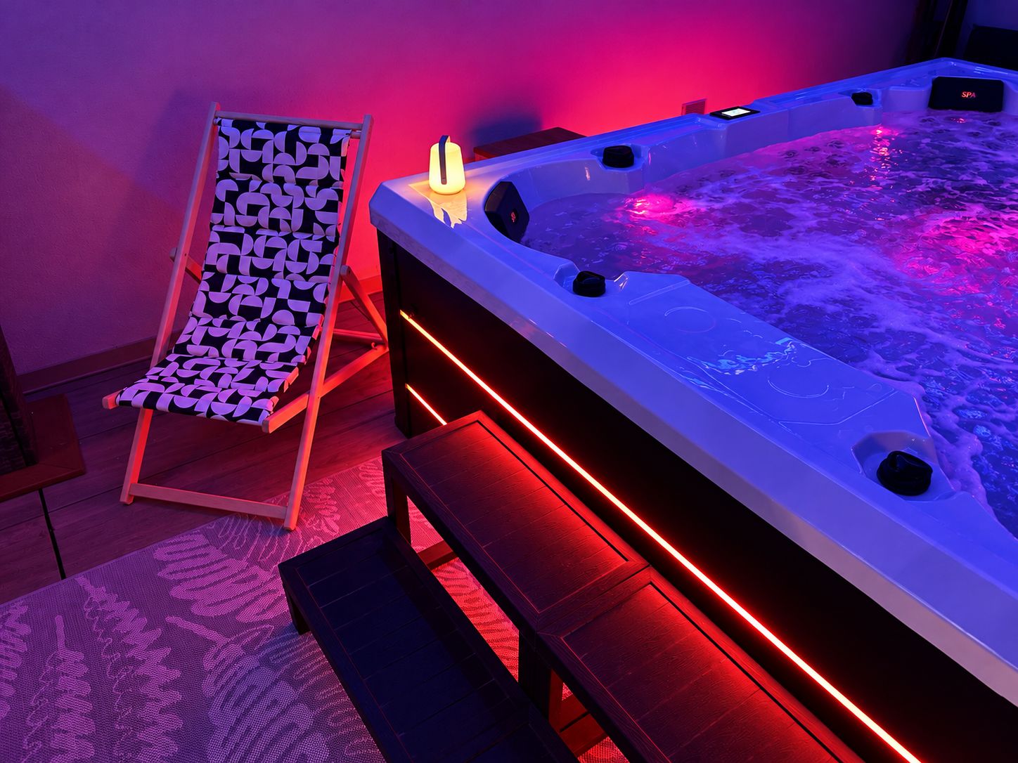 Un área de spa con un jacuzzi, una silla lounge estampada e iluminación ambiental roja.