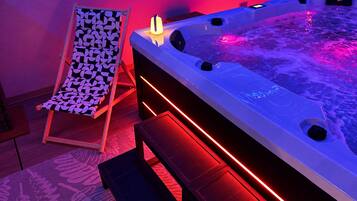 Un área de spa con un jacuzzi, una silla lounge estampada e iluminación ambiental roja.