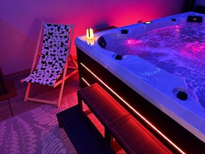 A spa area with a hot tub, a patterned lounge chair, and red ambient lighting.