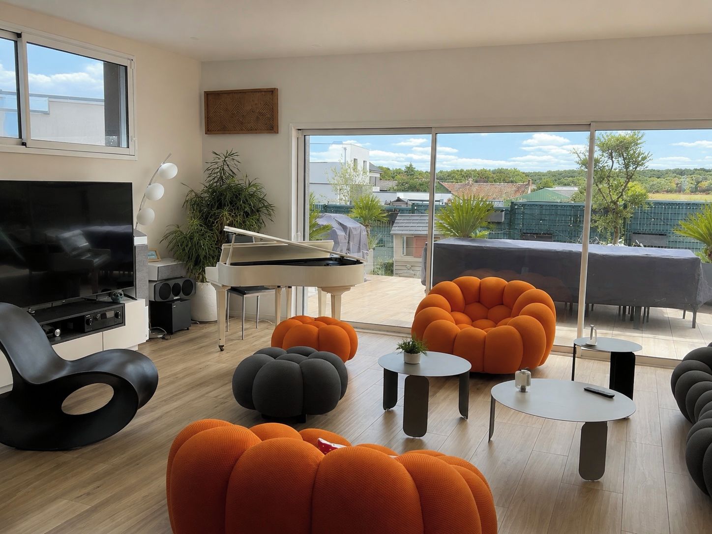 Un salon moderne avec un piano, un téléviseur et des poufs orange et gris.