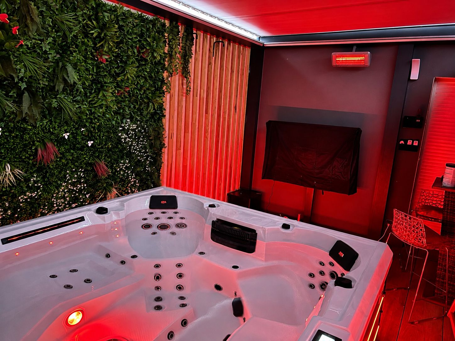 Un espace bien-être comprenant un jacuzzi, un téléviseur et un éclairage d’ambiance rouge.