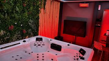 Un espace bien-être comprenant un jacuzzi, un téléviseur et un éclairage d’ambiance rouge.