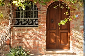 A brick building with a wooden double door and a metal gate. - Cetine Vecchie Farmstay – La Stalla (Torrita di Siena)