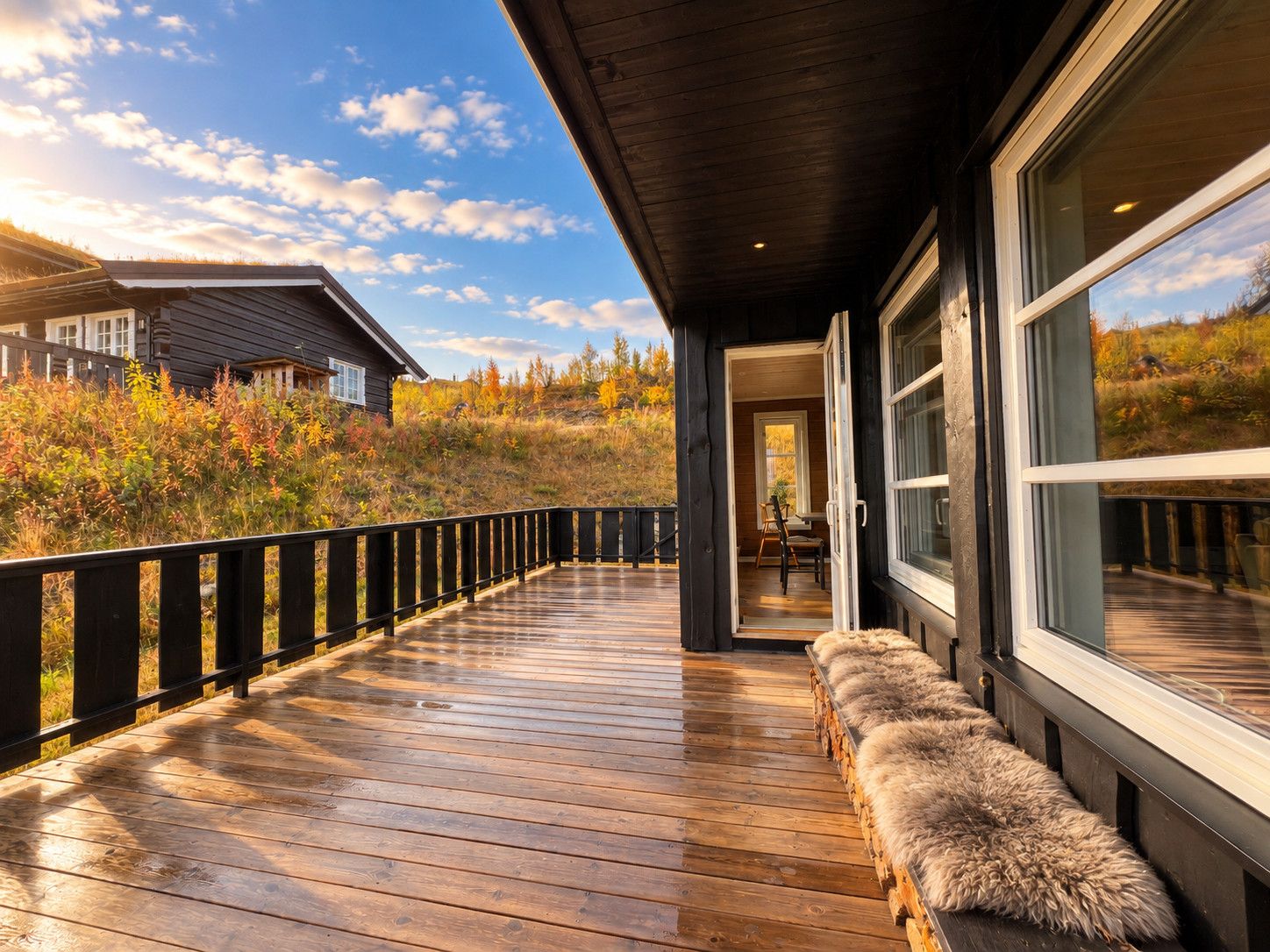 A wooden deck with a fur-lined bench, a glass door leading to a room, and a view of a house and autumn foliage.