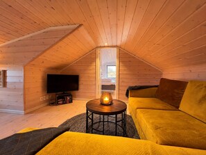 A cozy attic room with a wooden ceiling, a flat-screen TV, a sofa, and a table with a candle. - Mountain View at Gol Ski Resort with Sauna (Gol)