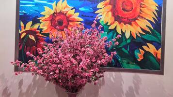 Quarto com uma grande pintura de girassóis e uma planta florida rosa em vaso.