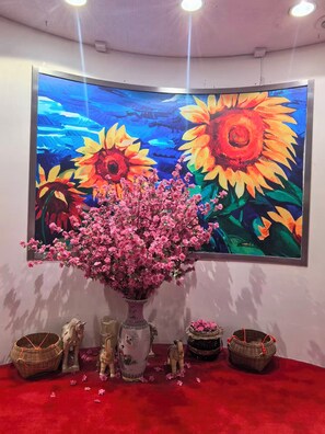 A room with a large painting of sunflowers and a pink flowering plant in a vase. - Tai Po Inn (N.T)