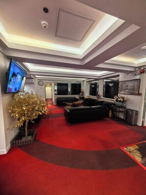 A modern living room with a red carpet, a black sofa, a flat-screen TV, and a decorative tree. - Tai Po Inn (N.T)