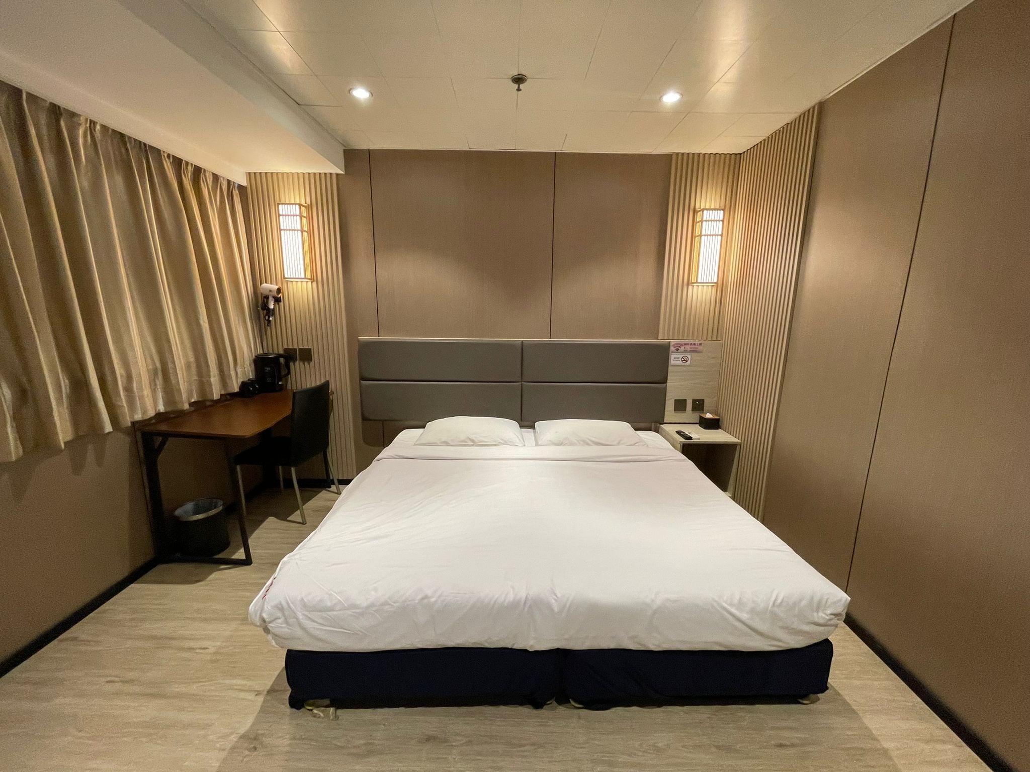Une chambre d’hôtel avec un grand lit, un bureau, une chaise, une machine à café et une table de chevet avec une télécommande.