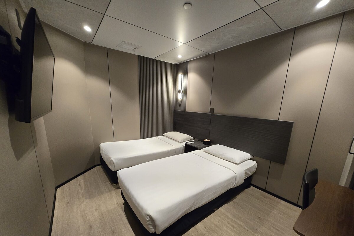A hotel room with two beds, a flat-screen TV mounted on the wall, and a wooden table.