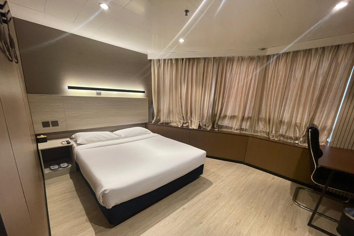 A modern hotel room with a large bed, a desk, and a window with curtains.