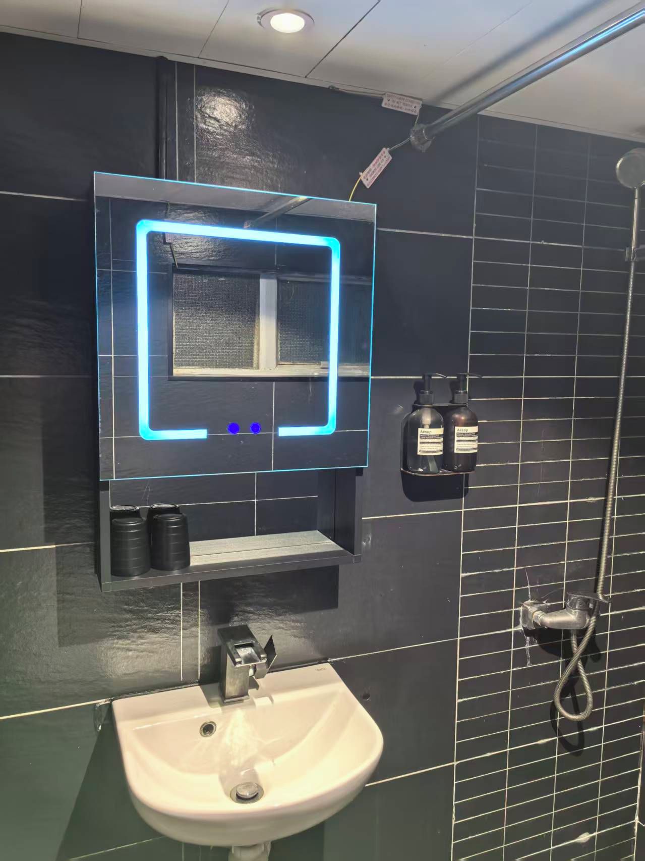 A bathroom with a white sink, a mirror with a neon light, and a shower.