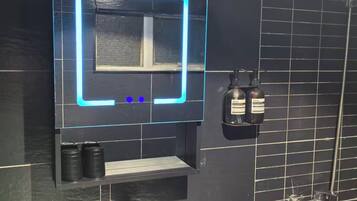 A bathroom with a white sink, a mirror with a neon light, and a shower.