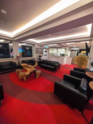 A modern lobby with a red carpet, black leather sofas, and a wooden coffee table. - Tai Po Inn (N.T)