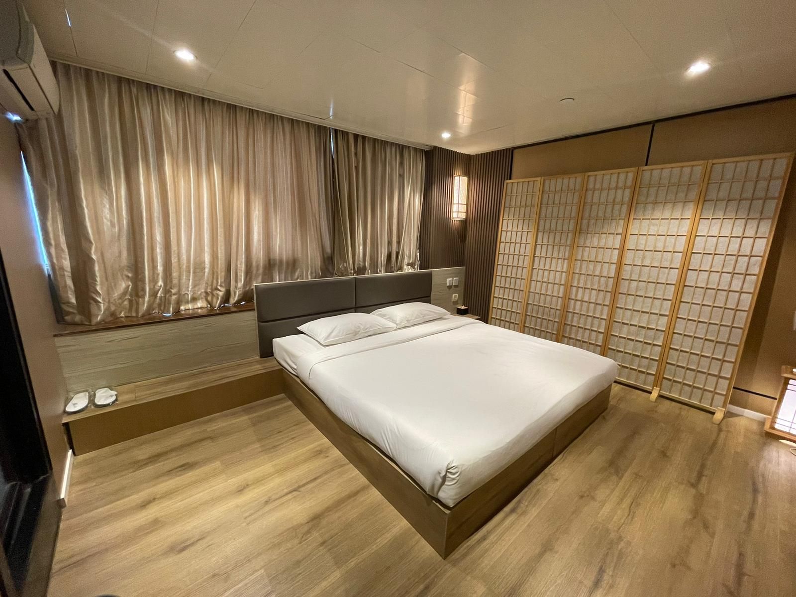 A modern bedroom with a large bed, wooden flooring, a headboard, and a shoji screen.