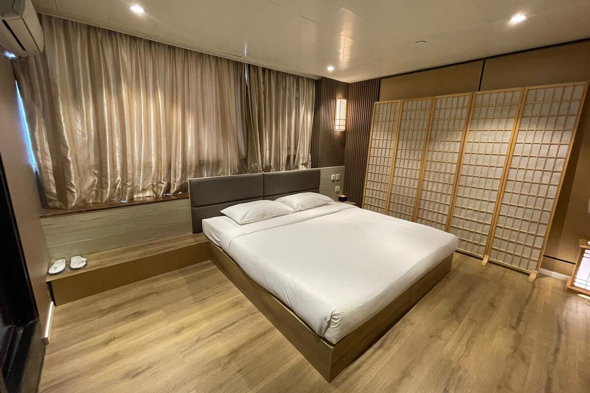 A modern bedroom with a large bed, wooden flooring, a headboard, and a shoji screen.