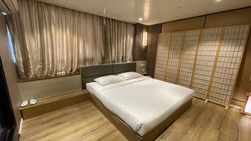A modern bedroom with a large bed, wooden flooring, a headboard, and a shoji screen.