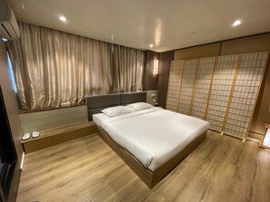 A modern bedroom with a large bed, wooden flooring, a headboard, and a shoji screen. - Tai Po Inn (N.T)
