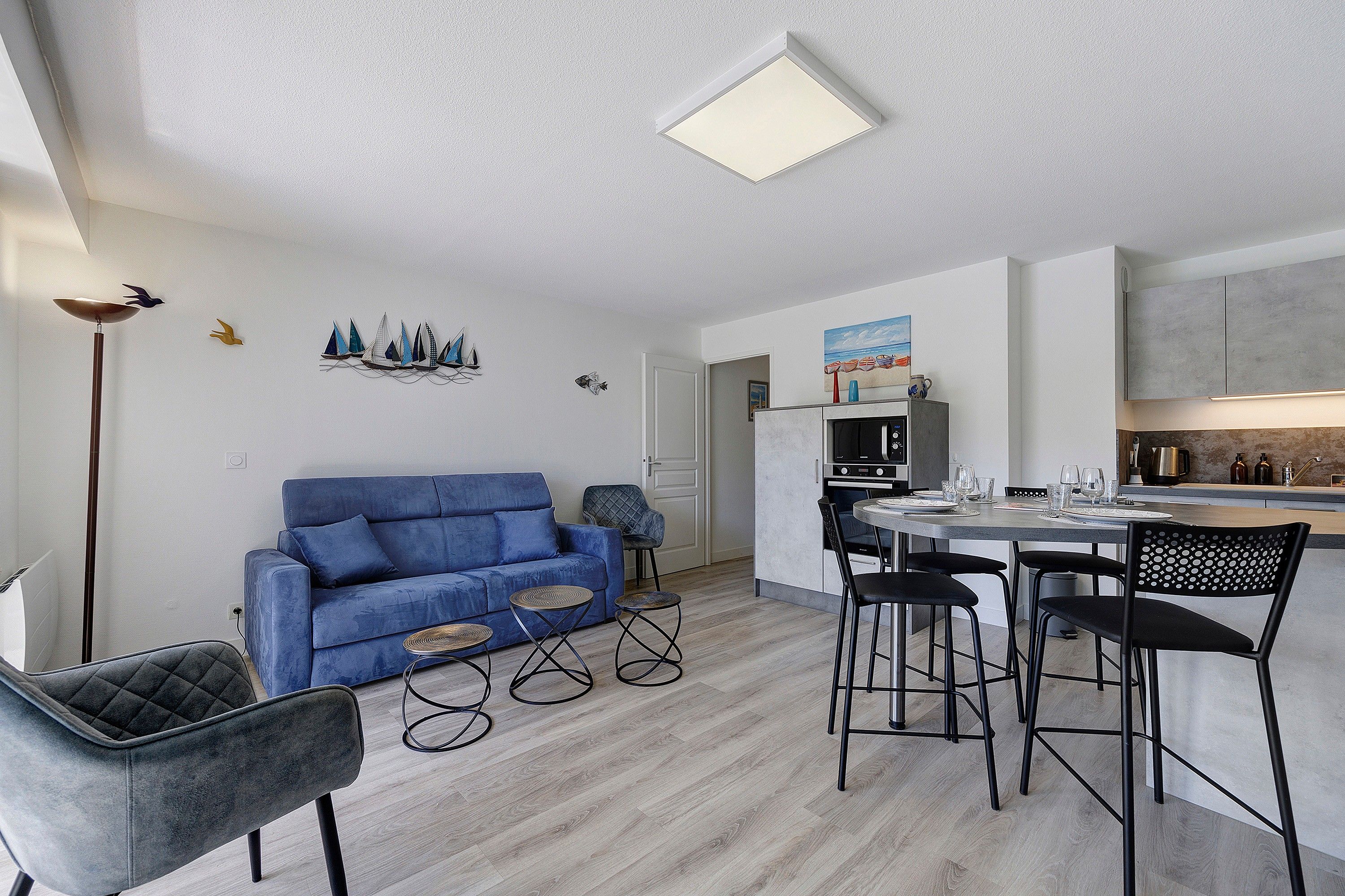 Een moderne woonkamer met een blauwe bank, een eethoek met een ronde tafel, en een keuken met een inbouwoven.